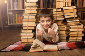 A child giving two thumbs up while lying on a checkered blanket surrounded by books. The background...