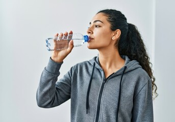 Young woman wearing sportswear drinking fresh water from plastic bottle after training