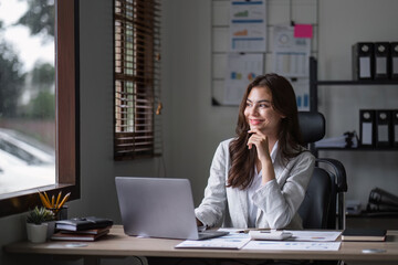 Young Businesswoman Analyzing Documents at Modern Office Desk with Laptop and Charts in Background