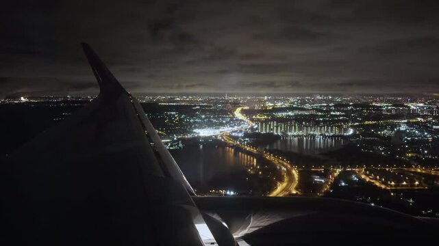 View from cabin of airplane with marker lights flying over night city. Flying a passenger plane low altitude over modern city with rivers and bridge. Business flights between cities Film grain texture