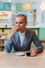 Professional businesswoman enjoying a coffee break in a modern cafe, dressed in a formal suit, taking a moment to relax and recharge during a busy workday; confident and focused, with smartphone