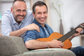 Fototapeta premium gay couple with guitar sitting on sofa at home