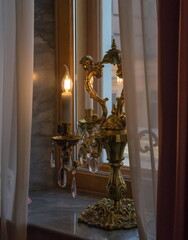 A candlestick with crystal pendants stands on the window in the semi-darkness