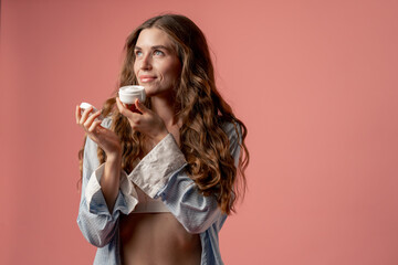 studio beauty shoot on pink background long-haired girl posing in underwear and blue shirt with jar...