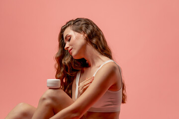 studio beauty shoot on pink background long-haired girl sitting posing in underwear with jar of...