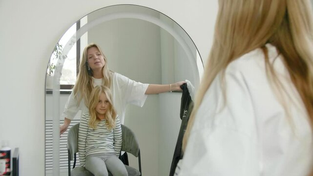 A hairstylist taking a black cape off from a girl after a haircut at a hair salon. First haircut. A satisfied client. Hair styling.