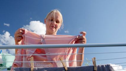 Woman hanging a pink striped shirt on an outdoor clothesline on a sunny day.