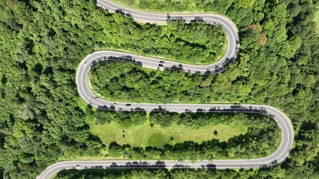 Drone flight in the mountains over a winding road with passing cars surrounded by a dense forest. Mavic 3