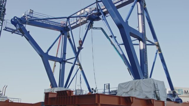 Beautiful wide view of a hook on a crane lowering while a pre-piling template is being constructed in the background. The piling template will be used to place offshore wind turbines in deep water