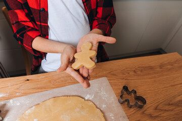 A little boy at a wooden table in the kitchen making cookies with cookie cutter in a shape of human. Top view