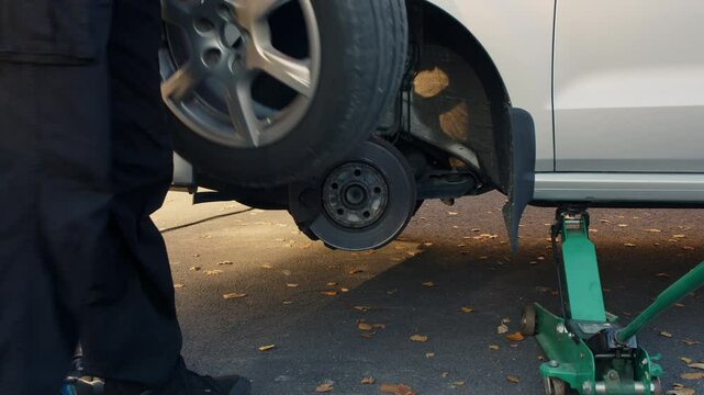 Auto Mechanic Man Changing Tire Outside Car, Removing Wheel and Revealing Brake Disc, Automotive Service, Hands Replacing Summer Tyres on Sunny Day in Autumn on Driveway, Garage