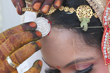 Indian wedding ritual where sindoor (vermilion) is being applied to the bride's hair parting, symbolizing the sacred bond of marriage.	