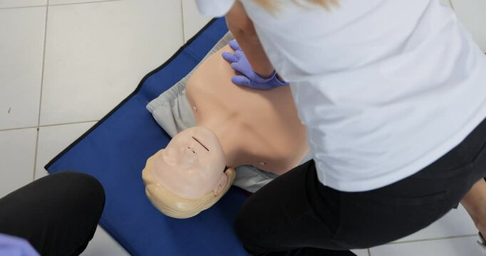 Young woman instructor showing how to make chest compressions with dummy during the first aid group training indoors.