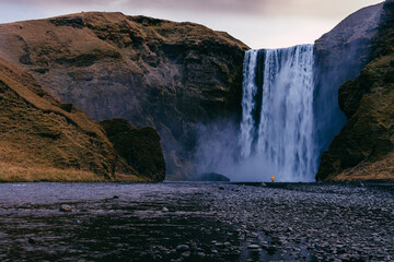 Skogafoss waterfall during sunrise with a person standing in yellow coat
