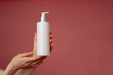 close up studio beauty shoot on a pink background female hands holding a white container with a dispenser for lotion beauty industry beauty salons