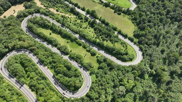 Drone flight in the mountains over a winding road with passing cars surrounded by a dense forest. Mavic 3