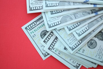 Big amount of hundred dollar bills in thick stack lies on bright red color paper background