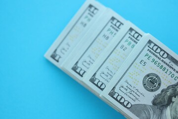 Big amount of hundred dollar bills in thick stack lies on bright blue color paper background