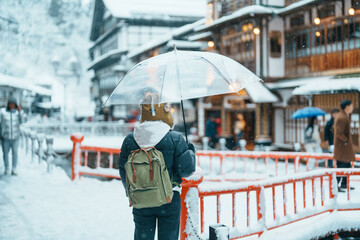 Fototapeta premium Woman tourist Visiting Ginzan Onsen in Yamagata, happy Traveler sightseeing Japanese Onsen village with Snow in winter season. landmark and popular for attraction in Japan. Travel and Vacation concept