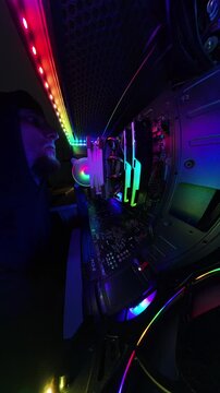 Vertical video. A man reaches inside a gaming PC to fix a problem, shown in a super wide-angle view with a "Tiny Planet" effect. The shot highlights the vibrant RGB lighting, cooling fans, and hardwar