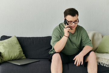 A thoughtful young man with Down syndrome speaks on the phone while sitting comfortably at home.