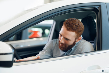 Portrait handsome happy bearded man in suit testing new car in showroom