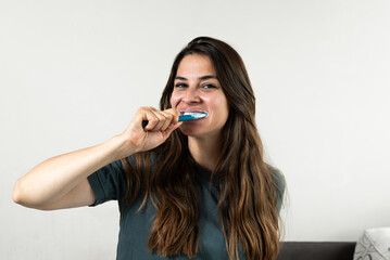 Smiling young woman brushing teeth in bathroom. Happy girl looking in mirror while using ecological toothbrush with whitening toothpaste. Beauty girl in bathroom cleaning teeth in the morning time.
