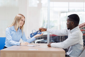 Fototapeta premium Happy owner young girl buys her first car, woman signs documents and receives keys at dealership