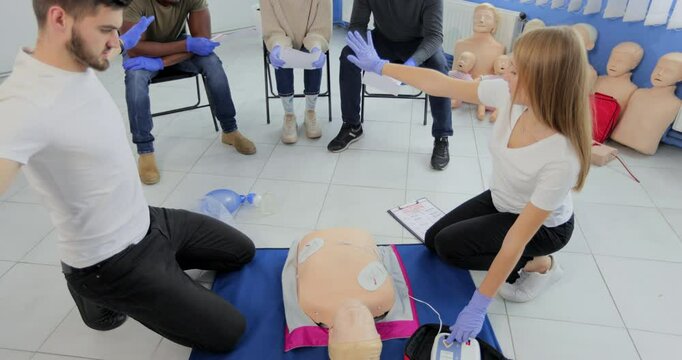 CPR training medical procedure workshop. Demonstrating chest compressions and use of AED automatic defibrillator on CPR doll.