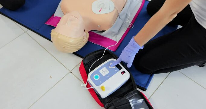 CPR training medical procedure workshop. Demonstrating chest compressions and use of AED automatic defibrillator on CPR doll