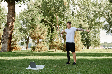 Tattooed young man working out in a park, engaging in an online fitness lesson with determination.