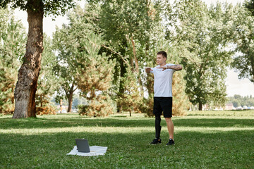 Tattooed young man trains in a park, engaging in an online fitness lesson with determination.
