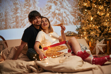 Delicious pizza. Beautiful young couple indoors, celebrating new year against projector