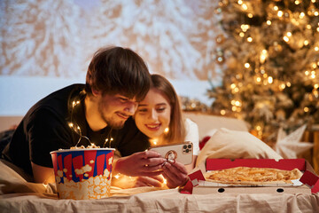 Taking photo by phone. Beautiful young couple indoors, celebrating new year against projector