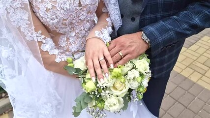 Hands of the newlyweds are joined together on a bouquet of flowers. Detail Close-up of the bride and groom,