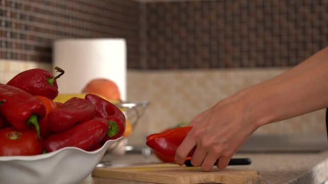 Hands of a young woman are cutting red peppers with a knife on a wooden board for further preparation in the kitchen. The concept of healthy eating, home cooking, a dull knife, sharpening a knife.