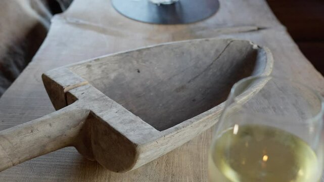 An antique wooden bailer rests on a rustic table inside restaurant, with a glass of wine in blurred foreground. Decorative, historical touch