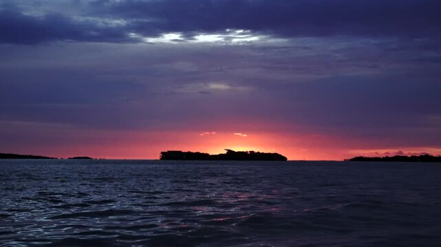 Handshot of intense colors sunset on sea hided island with birds flying above