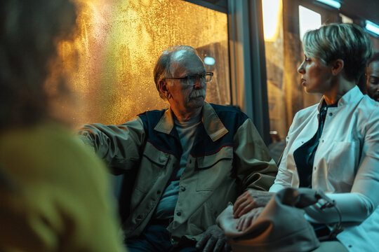 Older man talking to a woman on a bus at night