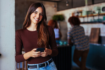 Woman in love standing in the kitchen doorway holding her phone and smiling at the camera