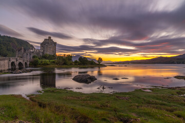 Obraz premium Eilean Donan Castle spiegelt sich bei Sonnenuntergang im Loch Duich, Langzeichtbelichtung erzeugt mit orangen und lila Wolken eine mystische Stimmung