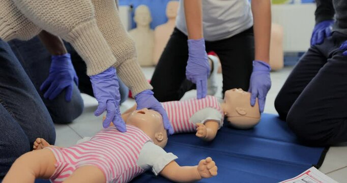 Close up of group of multiethnic people during the first aid training with instructor showing on manikin how to do artificial respiration for the baby.