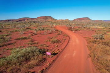 Aerial view of the scenic red earth landscape with a dirt road and rugged mountains, Nanutarra Road, Karijini National Park entrance, Pilbara Region, Australia.