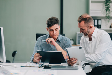 Two businessmen working together Analyze financial reports with charts and graphs while using the...