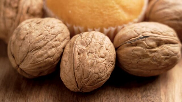 Fresh baked muffin surrounded by raw whole organic walnuts on a wooden surface, showcasing a natural wholesome snack. Close up. Rotation