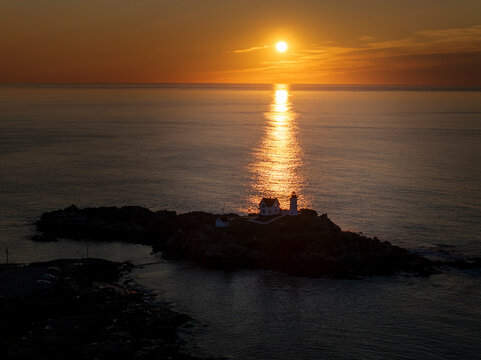 Aerial view of nubble lighthouse at sunrise over a serene ocean and rocky coastline, cape neddick, united states.