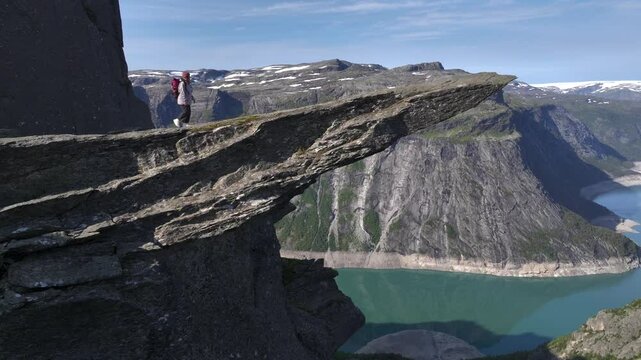 Girl with Backpack on the edge of cliff on Trolltunga, Norway. Aerial of Norwegiant Highlight SIghtseeing Troll Tongue