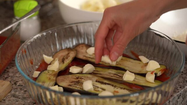 A young woman puts sliced ​​mozzarella on a plate and sprinkles with parmesan while preparing the southern classic dish parmigiana in the kitchen. Home cooking, healthy eating, fresh vegetables