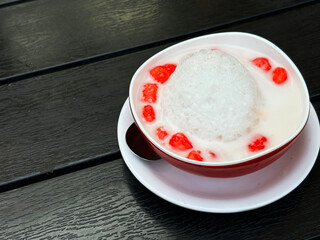 Thapthim krop or crispy ruby in Thailand language. The population one of an iced dessert in Thai food menu. The bowl of Thapthim krop on dark wooden table with space for text.