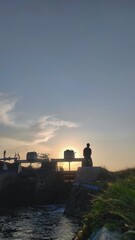 Fototapeta premium An unrecognised person stands amd taking picture on a water gate structure during sunset. The peaceful scene captures the calmness of dusk and the flow of water below